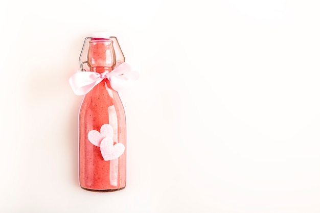 Foto glazen fles met verfrissende roze aardbeiensmoothie over melk met mooie harten en kopieerruimte. gezond, detox en dieetvoedselconcept. cadeau.