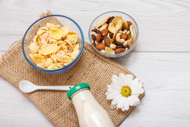 Glazen fles verse melk, kommen met muesli en cornflakes, kamillebloem op zak. bovenaanzicht.