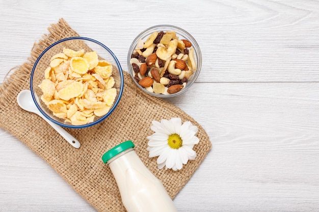 Glazen fles verse melk, kommen met muesli en cornflakes, kamillebloem op zak. Bovenaanzicht