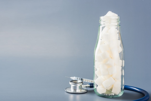 Glazen fles vol met witte suikerklontjes, zoet voedselingrediënt en doktersstethoscoop