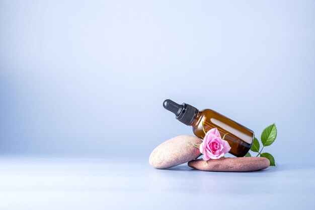 Glazen flesje met pipet voor een cosmetisch product met een roos op stenen