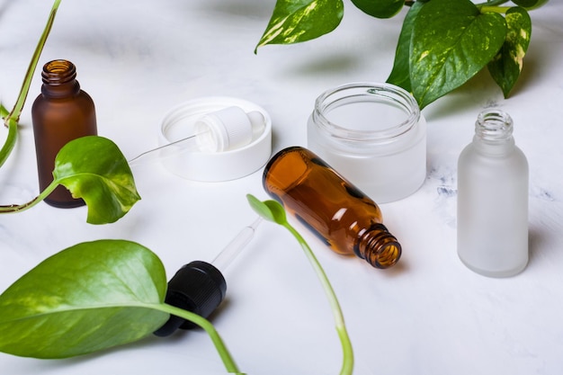 Glazen flessen en pot voor natuurlijke cosmetica op een witte marmeren achtergrond