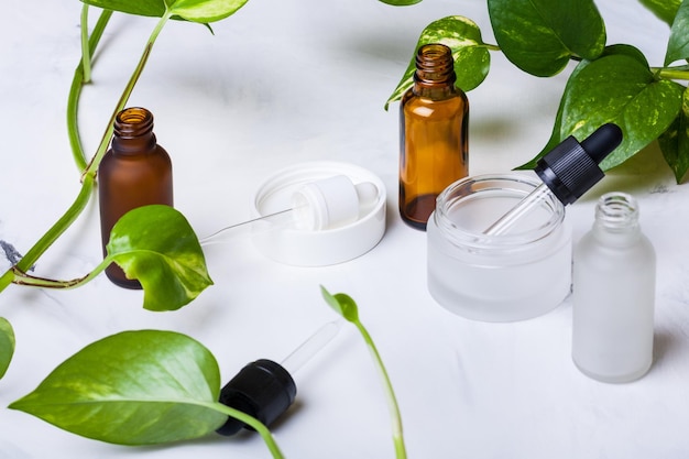 Glazen flessen en pot voor natuurlijke cosmetica op een witte marmeren achtergrond