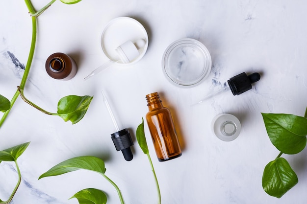 Glazen flessen en pot voor natuurlijke cosmetica op een witte marmeren achtergrond