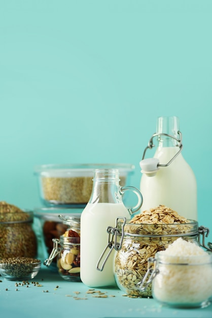 Glazen flessen vegan plantaardige melk en amandelen, noten, kokos, hennepzaad melk op blauwe achtergrond.