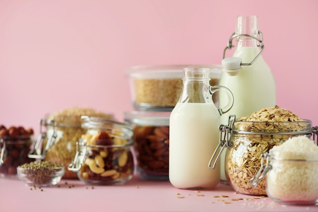 Glazen flessen vegan plantaardige melk en amandelen, noten, kokos, hennepzaad melk op roze achtergrond.