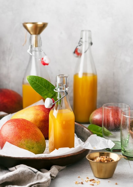 Glazen flessen vers fruitsap en rustieke metalen plaat met biologische mango's en kaarssuiker.