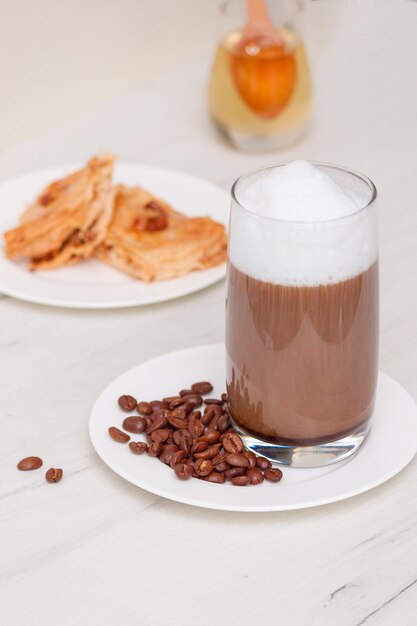 Glazen koffie met melkschuim met honing op witte houten tafel.