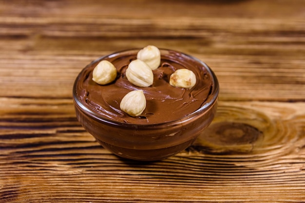 Glazen kom met chocopasta en hazelnoten op een houten tafel