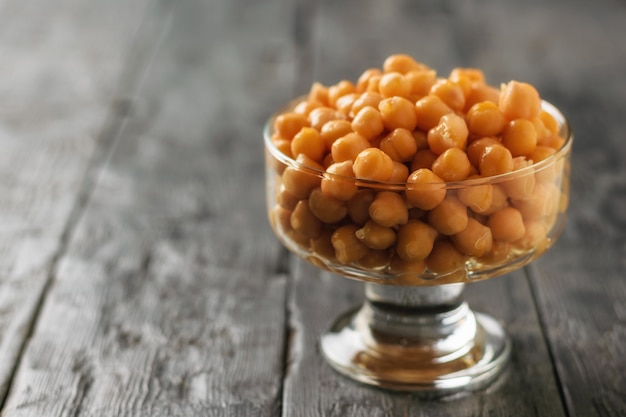 Glazen kom met gekookte kikkererwten op een donkere houten tafel. Vegetarische keuken van peulvruchten.