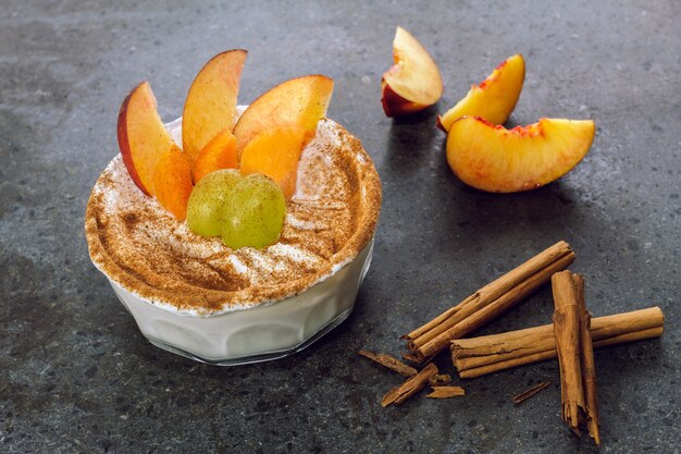 Glazen kom met griekse yoghurt, vers fruit en een snufje kaneel op een zwarte marmeren achtergrond.