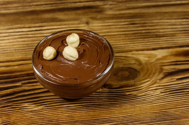 Glazen kom met heerlijke chocolade-hazelnootpasta op houten tafel