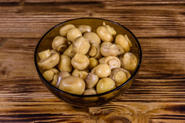 Glazen kom met ingeblikte champignons op houten tafel