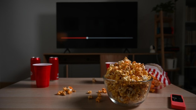 Glazen kom met popcorn en kopjes en afstandsbediening op houten tafel Familie vakantie recreatie ontspanning en hobby concept