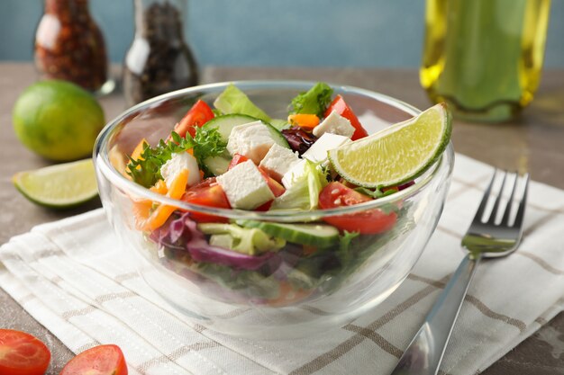 Glazen kom met salade, handdoek en kruiden op grijs