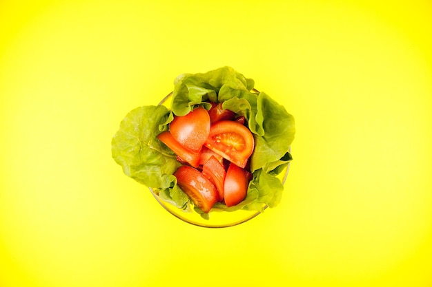 Glazen kom met saladebladeren en gesneden tomaten over gele achtergrond