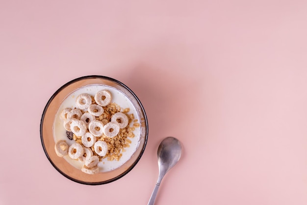 Glazen kom met yoghurt, muesli en ontbijtgranen op een beige achtergrond, kopieer ruimte