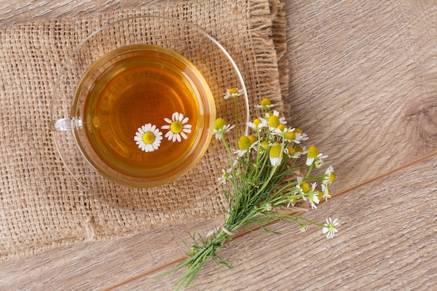 Glazen kopje groene thee met witte kamille bloemen op houten achtergrond. Bovenaanzicht