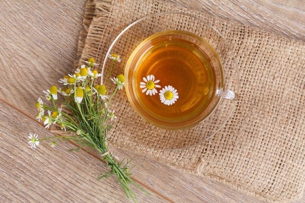 Glazen kopje groene thee met witte kamille bloemen op houten achtergrond. Bovenaanzicht