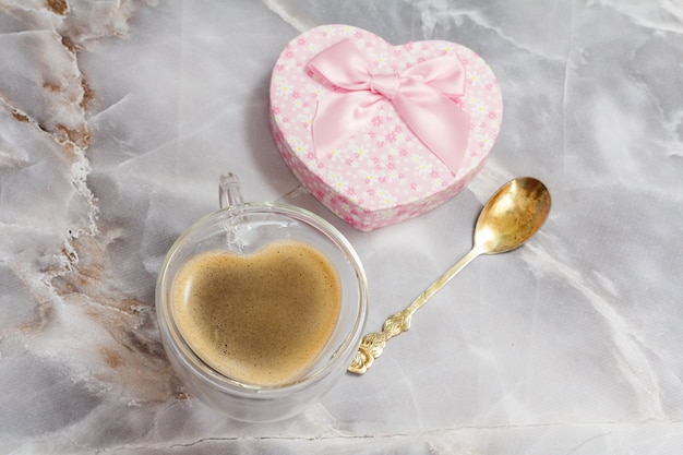 glazen kopje koffie, een lepel en een geschenkdoos op de keukentafel. de beker en de doos