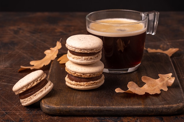 Glazen kopje koffie en chocolade macarons op houten achtergrond. Gezellige herfstcompositie - Afbeelding