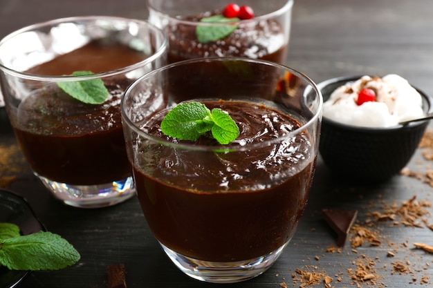 Glazen kopjes chocoladedessert met verse munt en opgeschuimde melk op zwarte houten tafel