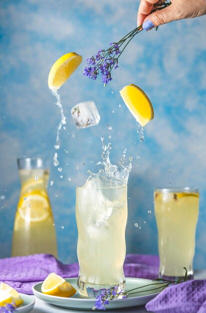 Glazen lavendellimonade met plons en vlieg citroenblokjesijs en lavendelbloemen in de hand van de vrouw op tafel in de zon zomer Close-up ondiepe scherptediepte