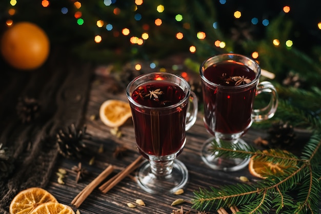 Glazen met glühwein op een houten tafel versierd met kerstbomen. Traditionele winter alcoholische drank met stukjes sinaasappel