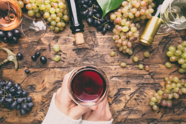 Glazen met witte, rode en roze wijn en rijpe druiven op houten ondergrond, bovenaanzicht. dameshand met wijnglas