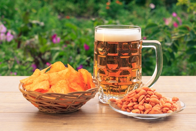 Glazen mok bier op houten tafel met chips in rieten mand, pinda's in plaat