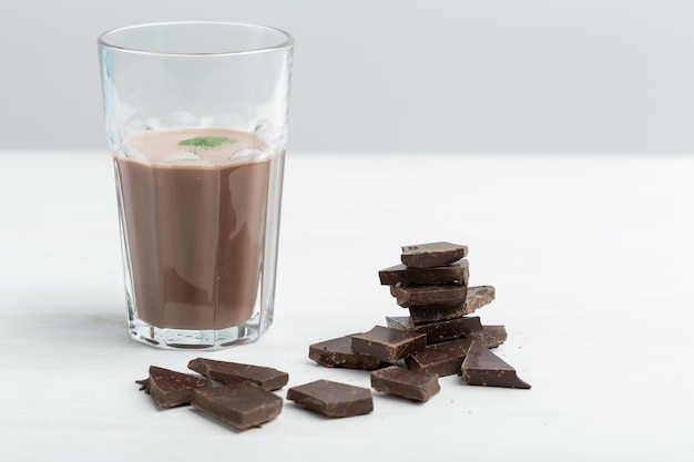 Glazen mok met een eiwitchocoladeshake staat tegen de achtergrond van een pakje eiwit op een witte tafel. Sportvoeding concept.