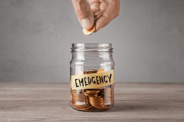 Glazen noodpot met munten en een inscriptie Emergency Man houdt munt in zijn hand