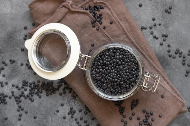 Glazen pot droge zwarte linzenbonen op grijs tafelblad, gezond eiwitdieet