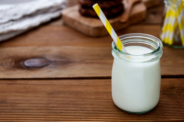 Glazen pot, fles witte melk op een houten achtergrond met een papieren rietje