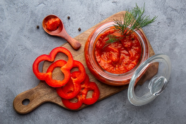 Glazen pot met ajvar, lutenitza op een grijze ruimte