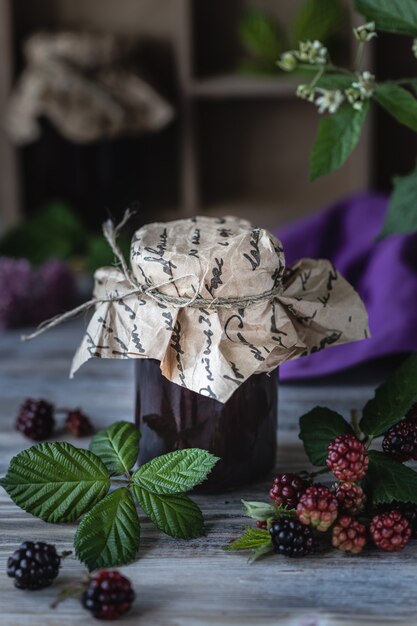 Glazen pot met BlackBerry saus close-up. Tak met bessen en bladeren in een houten gesneden doos op een donkere houten achtergrond.