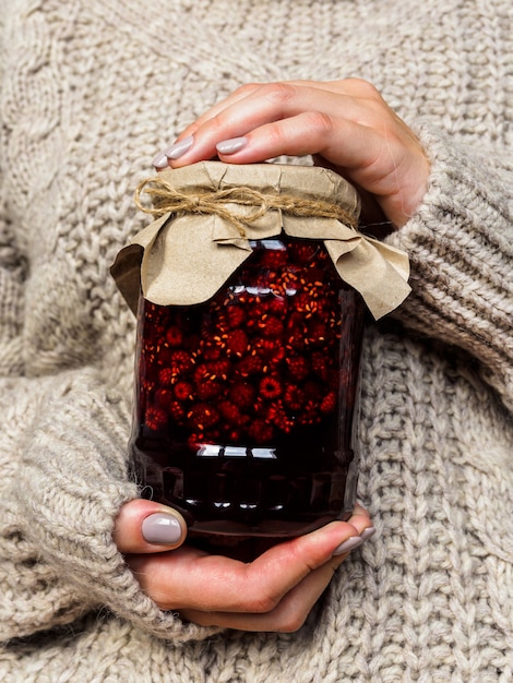 Glazen pot met frambozenjam in de handen van meisjes