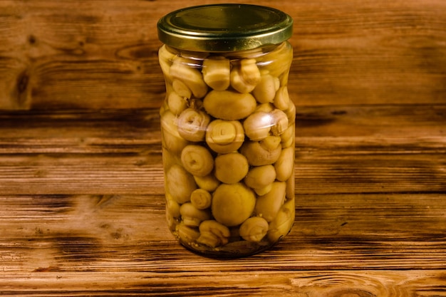 Glazen pot met ingeblikte champignons op rustieke houten tafel