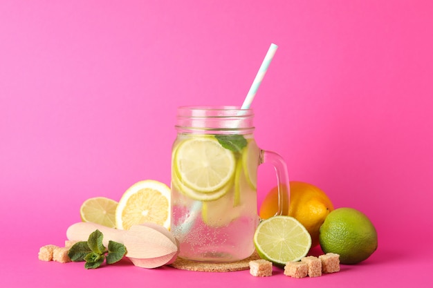 Glazen pot met limonade en ingrediënten op roze oppervlak