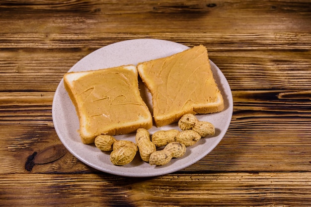 Glazen pot met pindakaas en bord met sandwiches op een houten tafel