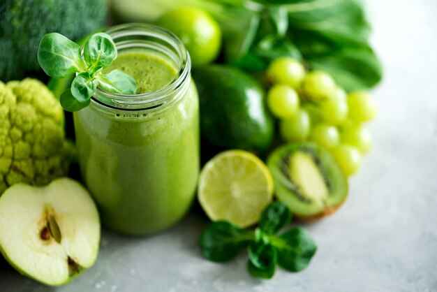 Glazen pot mokken met groene gezondheid smoothie, boerenkool bladeren, limoen, appel, kiwi, druiven, banaan, avocado, sla.