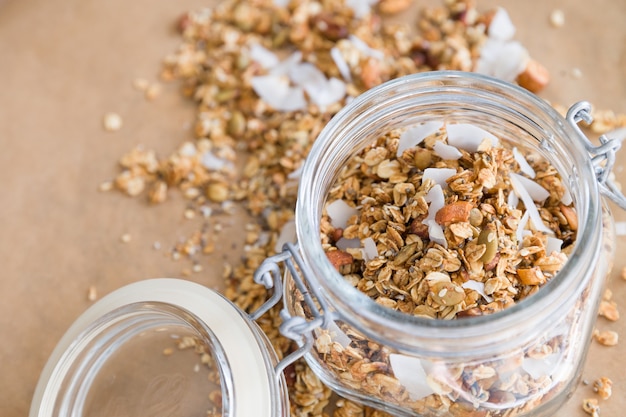 glazen pot zelfgemaakte biologische granola met kokos en pecannoten op de achtergrond van bakpapier