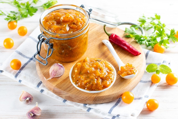 Glazen pot zelfgemaakte DIY natuurlijke ingeblikte gele kersenpruimensaus chutney met chili of tkemali staande op tafel, selectieve focus.