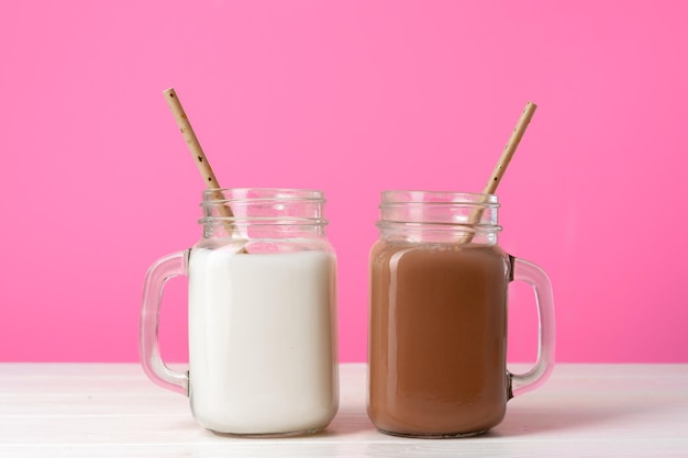 Glazen potten met gearomatiseerde milkshakes tegen roze achtergrond