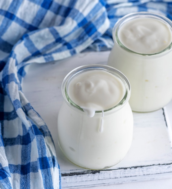 Glazen potten met zelfgemaakte yoghurt op een witte houten bord