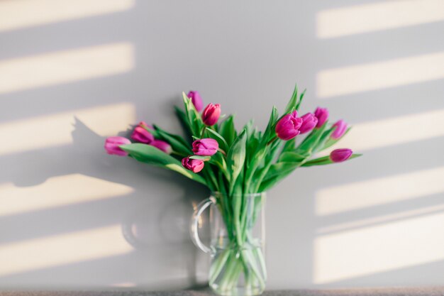 Glazen vaas met boeket van mooie tulpen op grijze muur muur