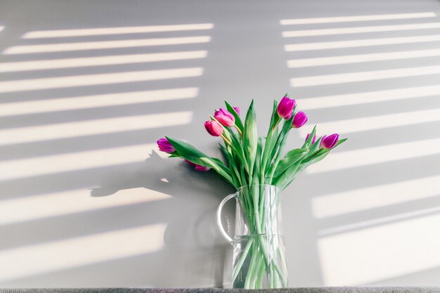 Glazen vaas met boeket van prachtige tulpen op grijze muur achtergrond