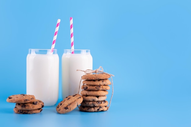 Glazen verse melk met stro en bruine schoolchocoladekoekjes op blauwe achtergrond