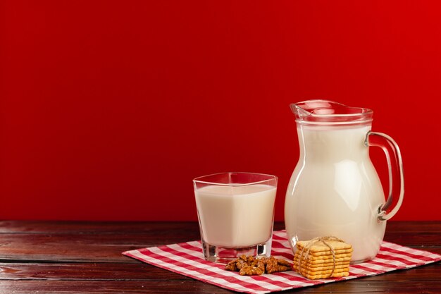 Glazen werper en kopje melk tegen rode achtergrond met koekjes