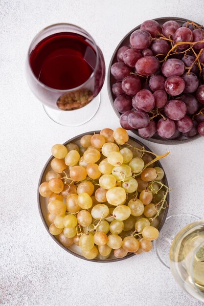 Glazen witte en rode wijn met rijpe druiven op een lichte stenen ondergrond
